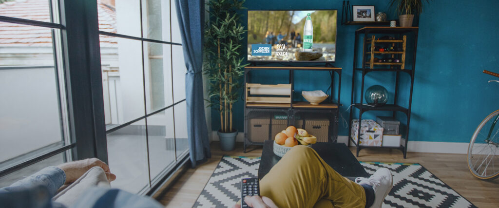Wohnzimmer mit Fernseher auf dem ein Jochen Schweizer Werbespot in Kooperation mit Vilsa läuft