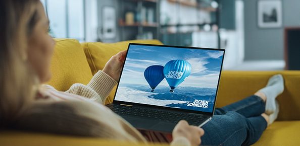 Person auf dem Sofa mit Laptop auf dem ein Jochen Schweizer Werbespot läuft