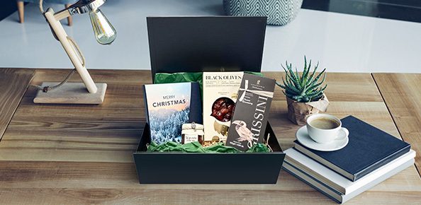 Jochen Schweizer Präsentbox auf Schreibtisch gefüllt mit Feinkost und einem Erlebnisgutschein in der Geschenkbox "Merry Christmas"
